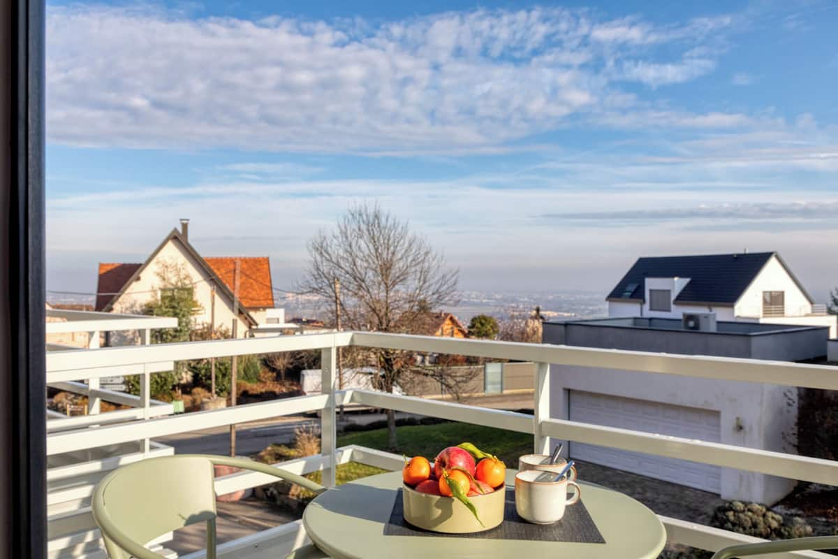 A balcony with a table, a bowl of fruit, and a cup.