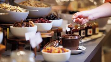 A buffet with various food items including bowls of cereal, fruit, and a chocolate spread.