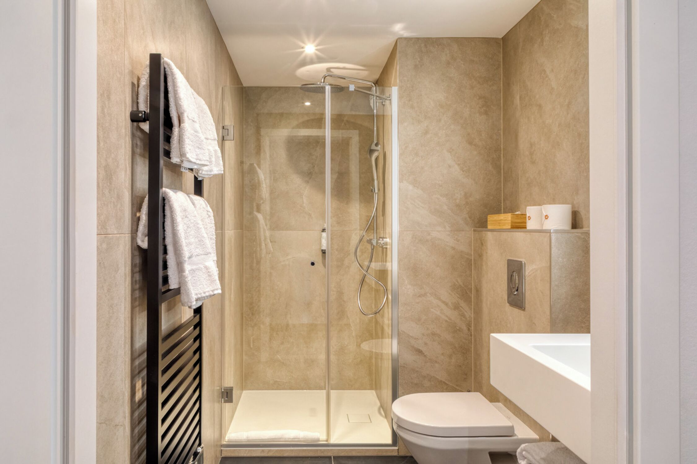 Un baño moderno con ducha envuelta en vidrio, inodoro blanco y tocador con lavamanos.
