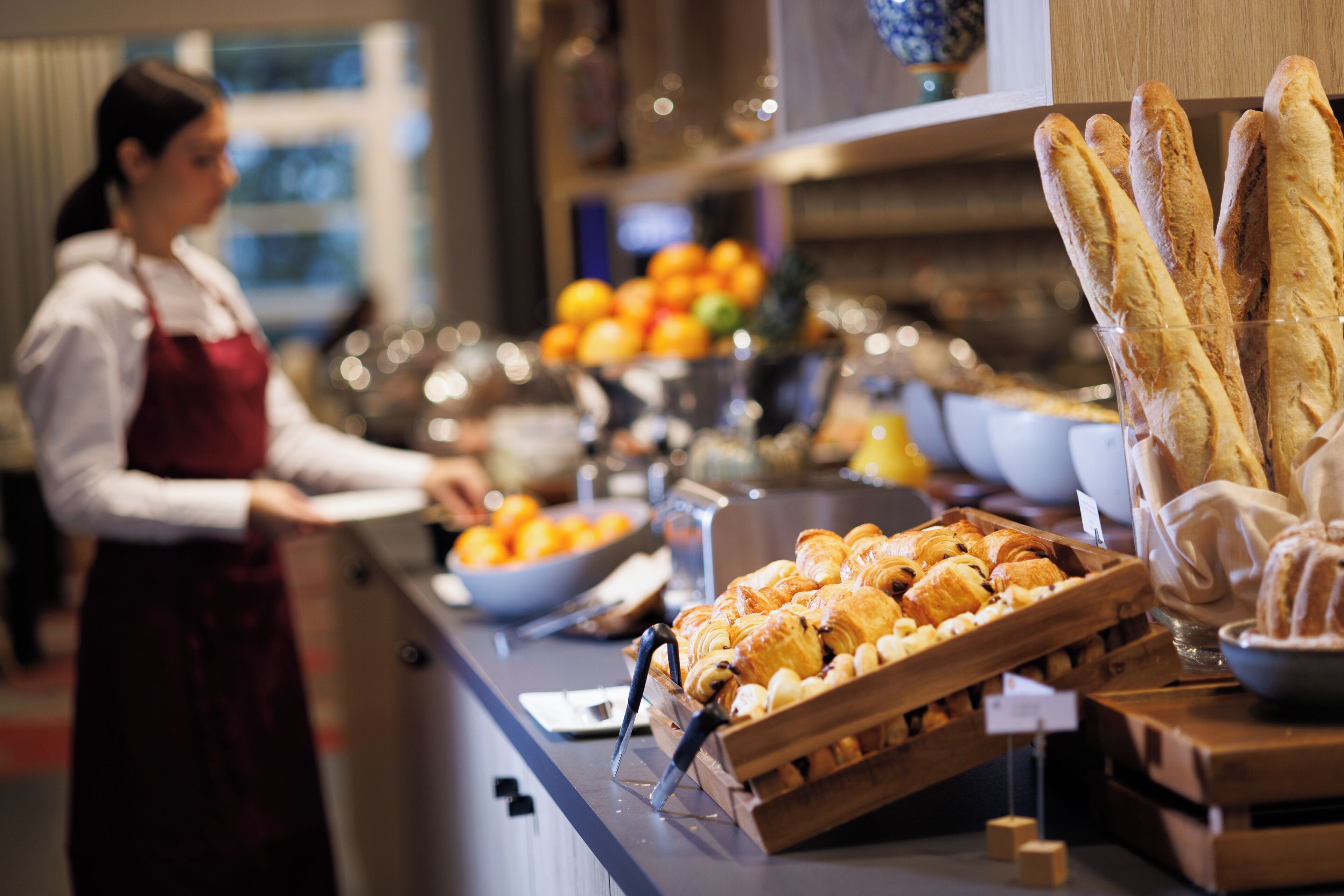 A buffet setup with various food items including bread, pastries, and fruits.