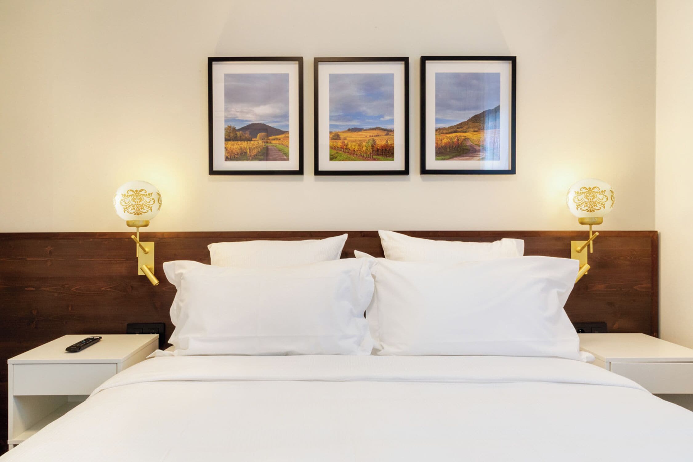 A hotel room with a large bed, two bedside tables, and three framed pictures on the wall.