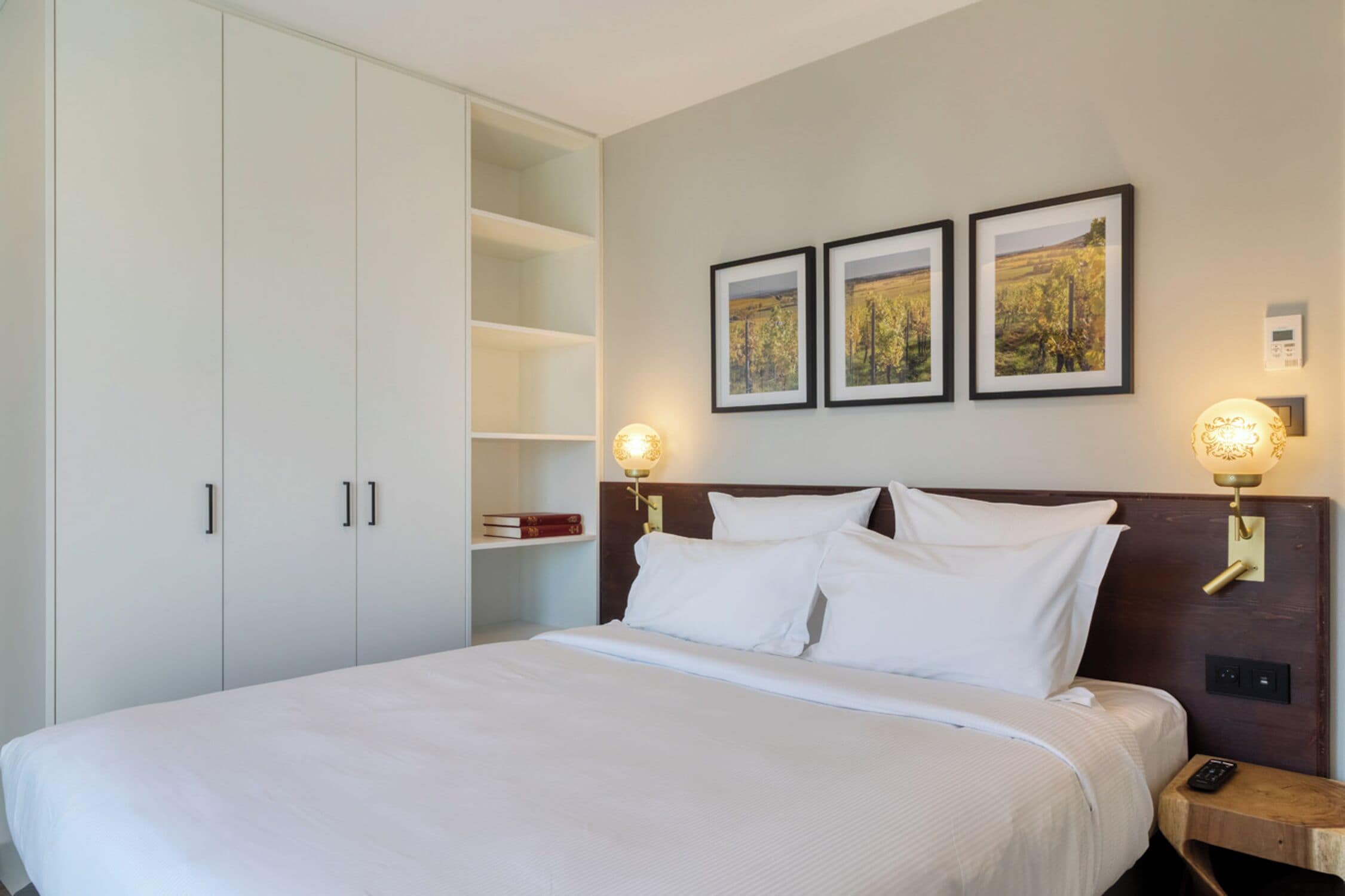 Een hotelkamer met een groot bed, een kledingkast, een nachtkastje met een lamp en drie ingelijste foto's aan de muur.