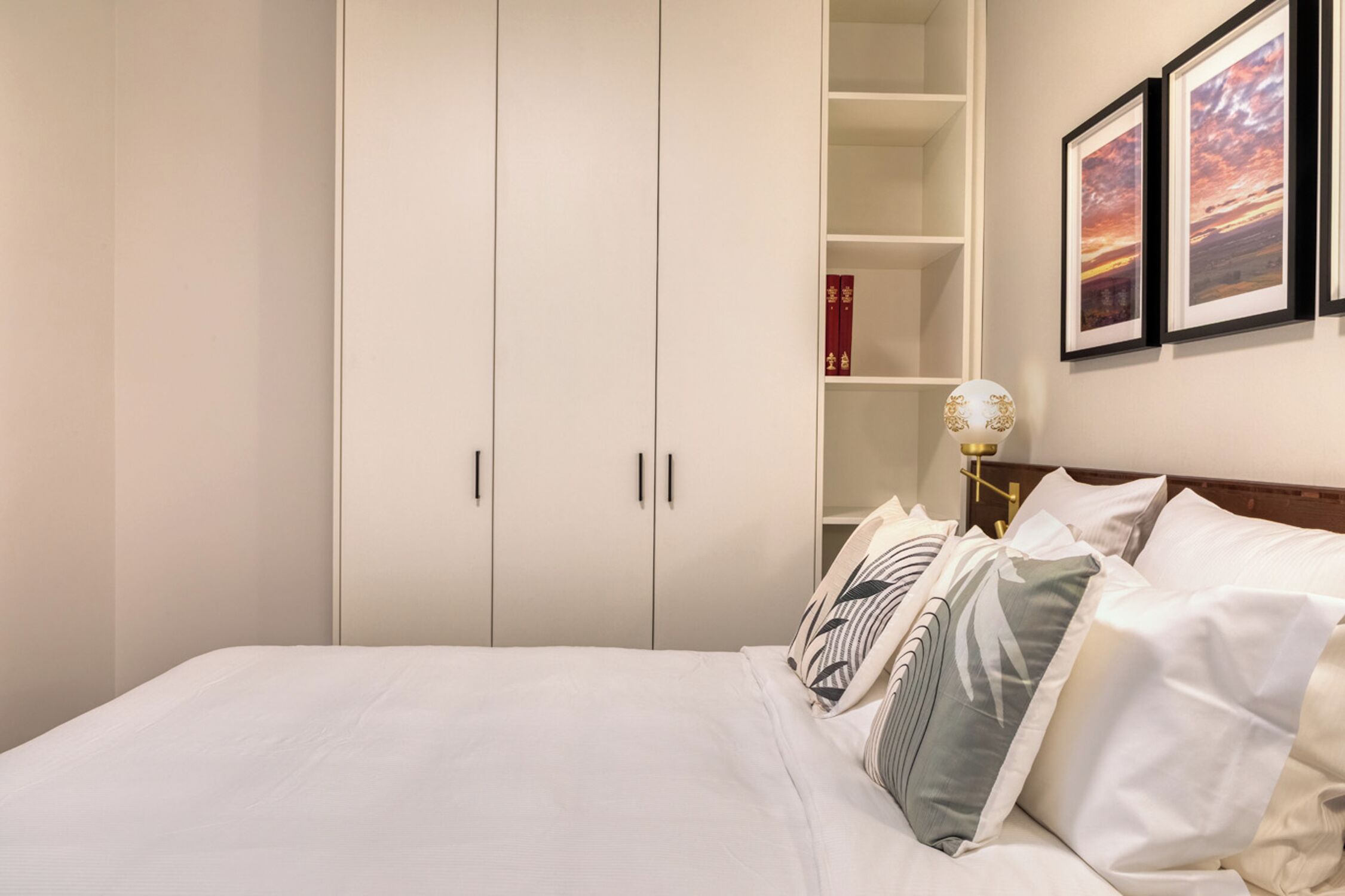 Ein ordentlich eingerichtetes Schlafzimmer mit einem Bett, einem weißen Kleiderschrank und gerahmten Bildern an der Wand.