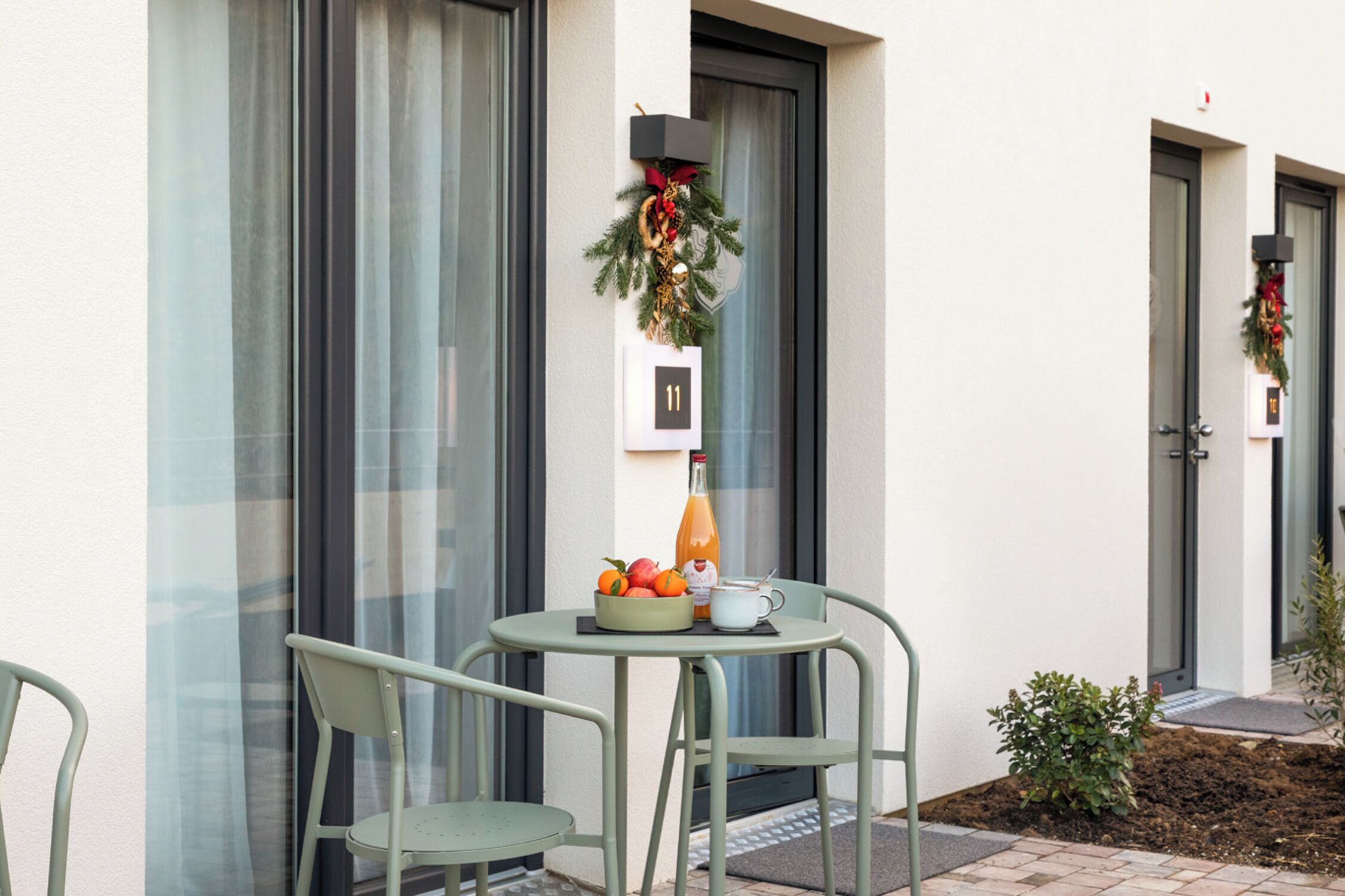 Een klein terras met een tafel, stoelen, een fruitschaal, een fles en een beker.