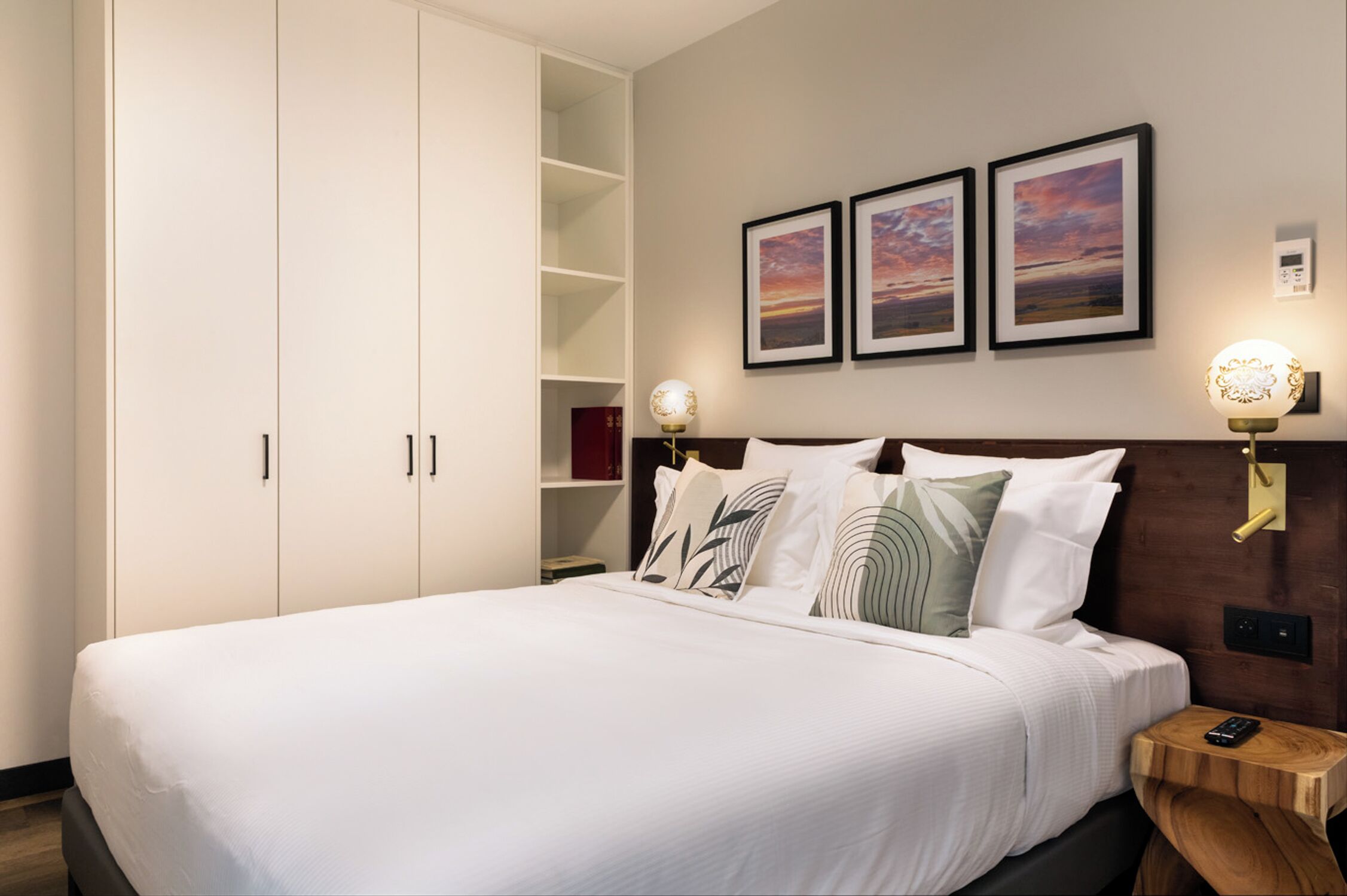 A neatly made bed with white linens, a wooden headboard, and three framed pictures on the wall.