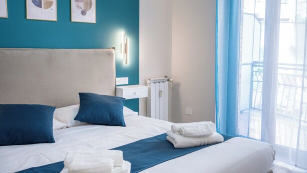 A neatly made bed with blue and white bedding, a white headboard, and a blue accent wall with framed artwork. - C&P Luxury Guest House Rome (Rome)