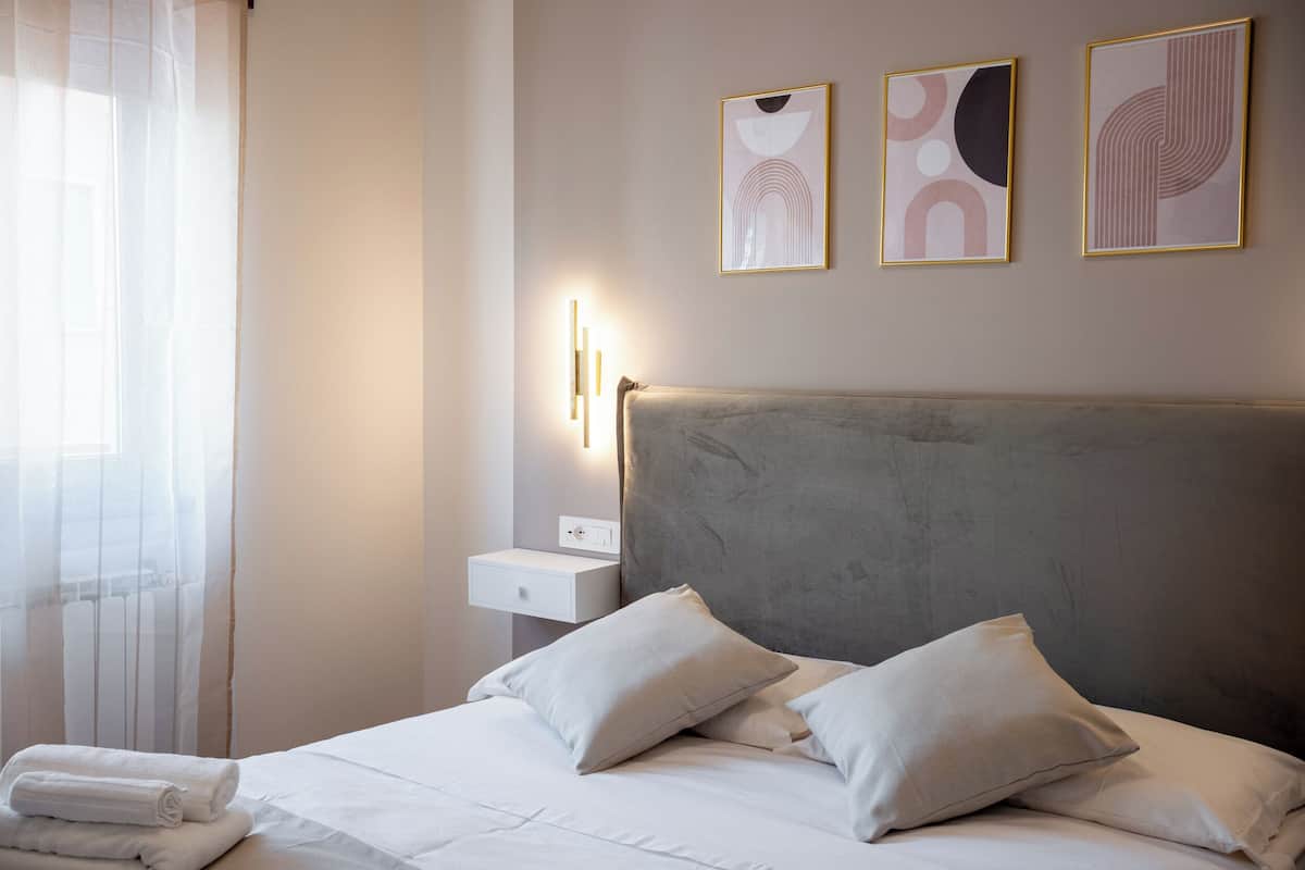 A neatly made bed with pillows, a bedside table with a lamp, and artwork on the wall.