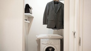 A laundry room with a washing machine, a hanging coat, and a shelf with a bag. - C&P Luxury Guest House Rome (Rome)