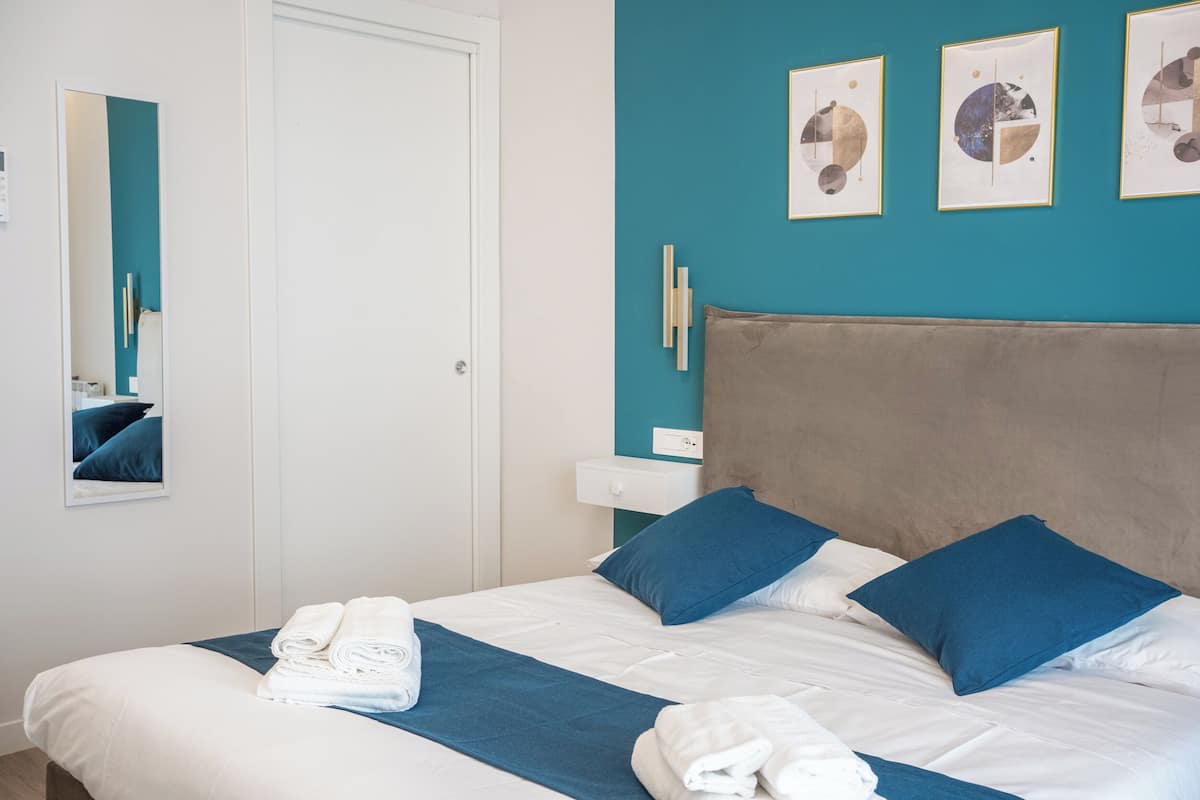 A neatly made bed with blue and white bedding, a teal accent wall, and framed artwork above the bed.
