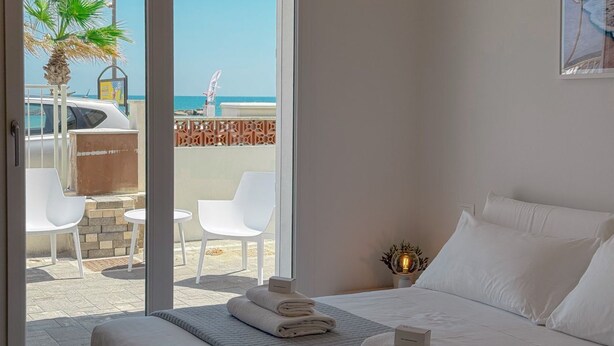 A hotel room with a bed, a small table with chairs, a view of the beach, and a palm tree. - Seafront & Reserved Parking (Civitanova Marche)