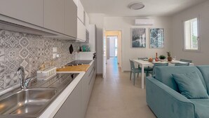 A modern kitchen with a large sink, white cabinets, and patterned backsplash. There is a dining area with a table and chairs, and a teal sofa. - Seafront & Reserved Parking (Civitanova Marche)