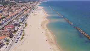 A coastal cityscape with a wide beach, a clear blue sea, and a distant mountain. - Seafront & Reserved Parking (Civitanova Marche)