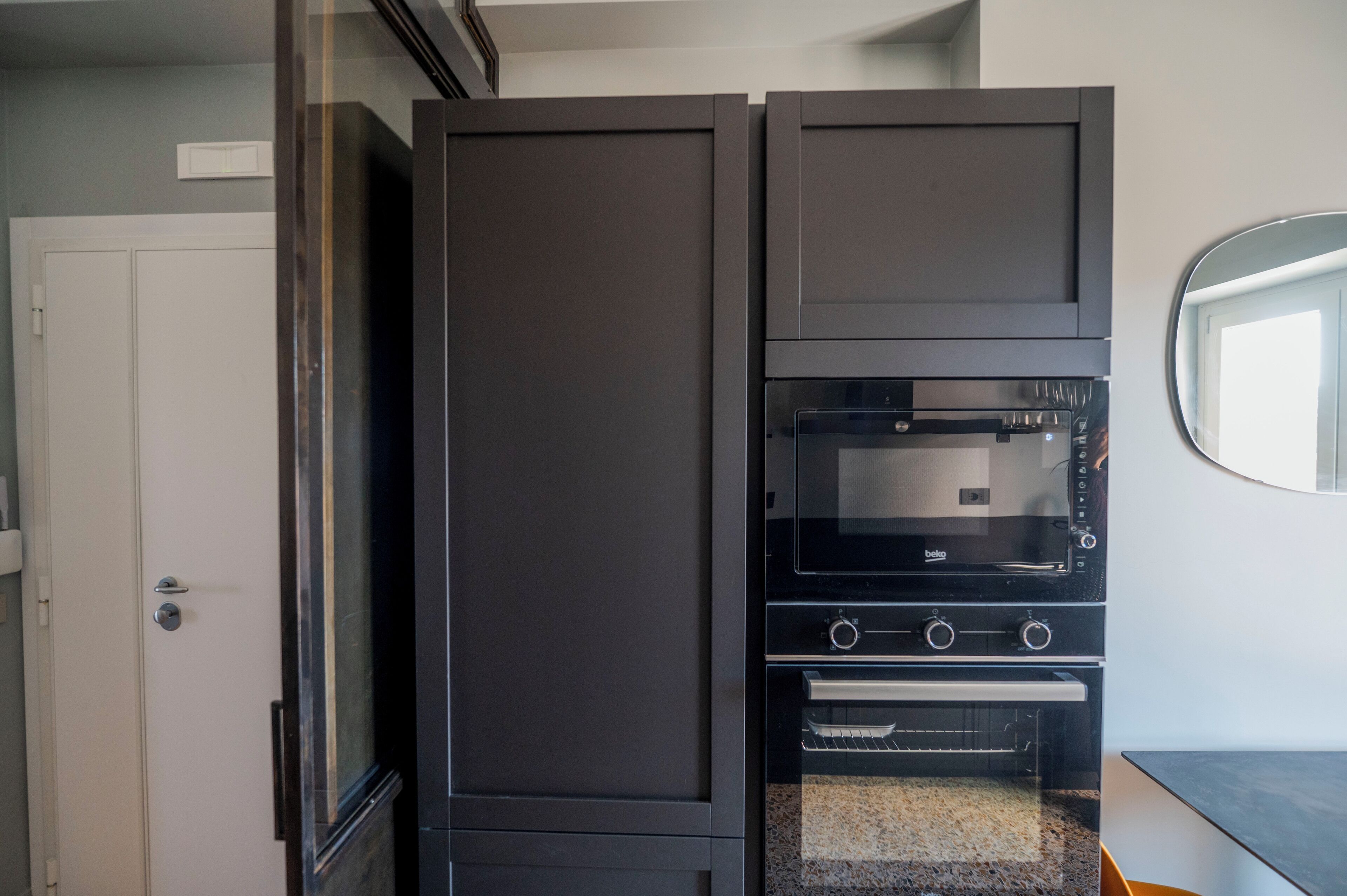 Een compacte keuken met een ingebouwde oven en magnetron, een deur en een klein aanrecht.