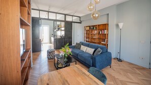 A modern living room with a blue sofa, wooden shelves, a coffee table with a vase, and a floor lamp. - Terrace Apartment Monte del Gallo (Rome)