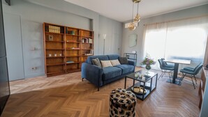 A living room with a blue sofa, wooden bookshelf, and a dining area with a table and chairs. - Terrace Apartment Monte del Gallo (Rome)