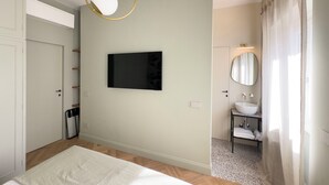 A modern bedroom with a bed, a mounted TV, a bedside table, and a bathroom with a sink and mirror. - Terrace Apartment Monte del Gallo (Rome)
