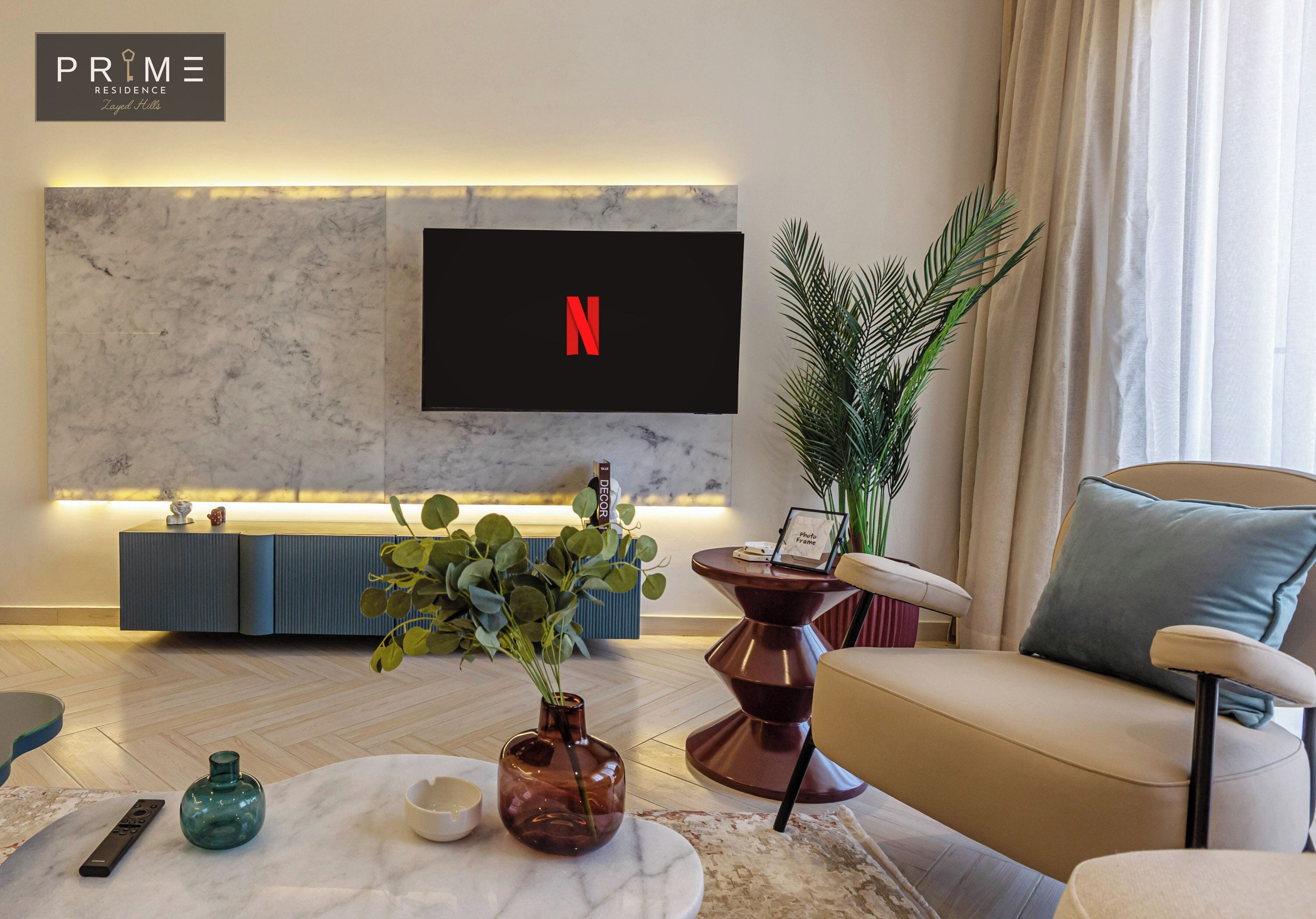 Una sala de estar moderna con una pared de mármol, un televisor montado que muestra el logotipo de Netflix, un sofá, una mesa de centro y una mesita auxiliar con una planta.