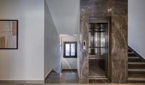 A modern interior with a marble staircase, a digital elevator display, and a framed abstract artwork on the wall. - Prime Residence Zayed Hills (Sheikh Zayed City)