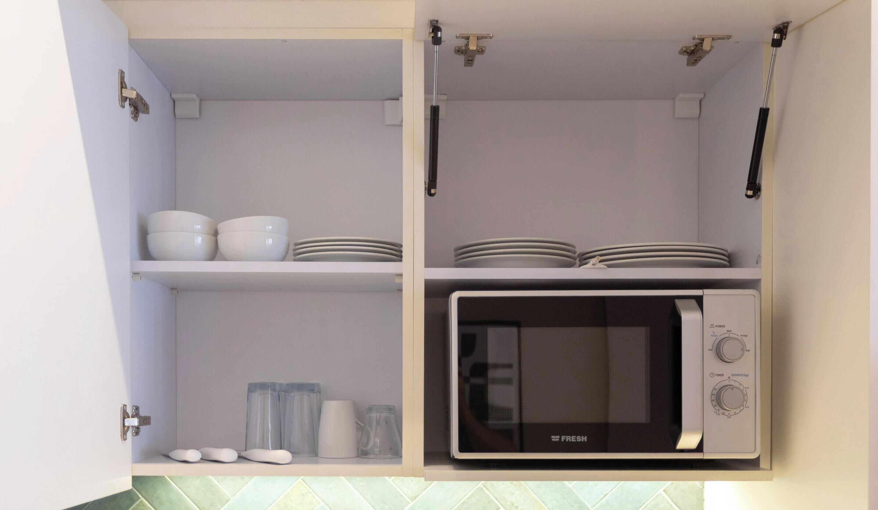 Une cuisine avec des meubles blancs, un four à micro-ondes et des étagères remplies de vaisselle.