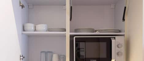 Une cuisine avec des meubles blancs, un four à micro-ondes et des étagères remplies de vaisselle.