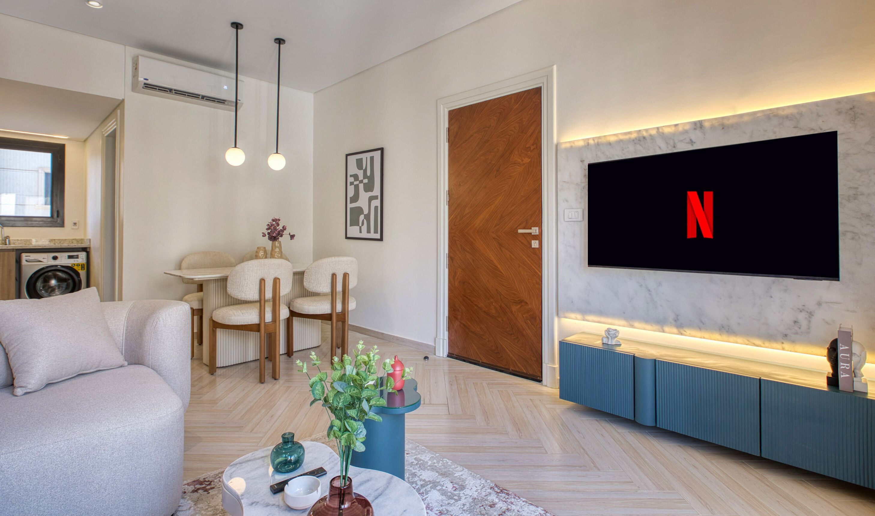 A modern living room with a flat-screen TV mounted on a marble wall, a sofa, a coffee table with decorative items, and a wooden door.