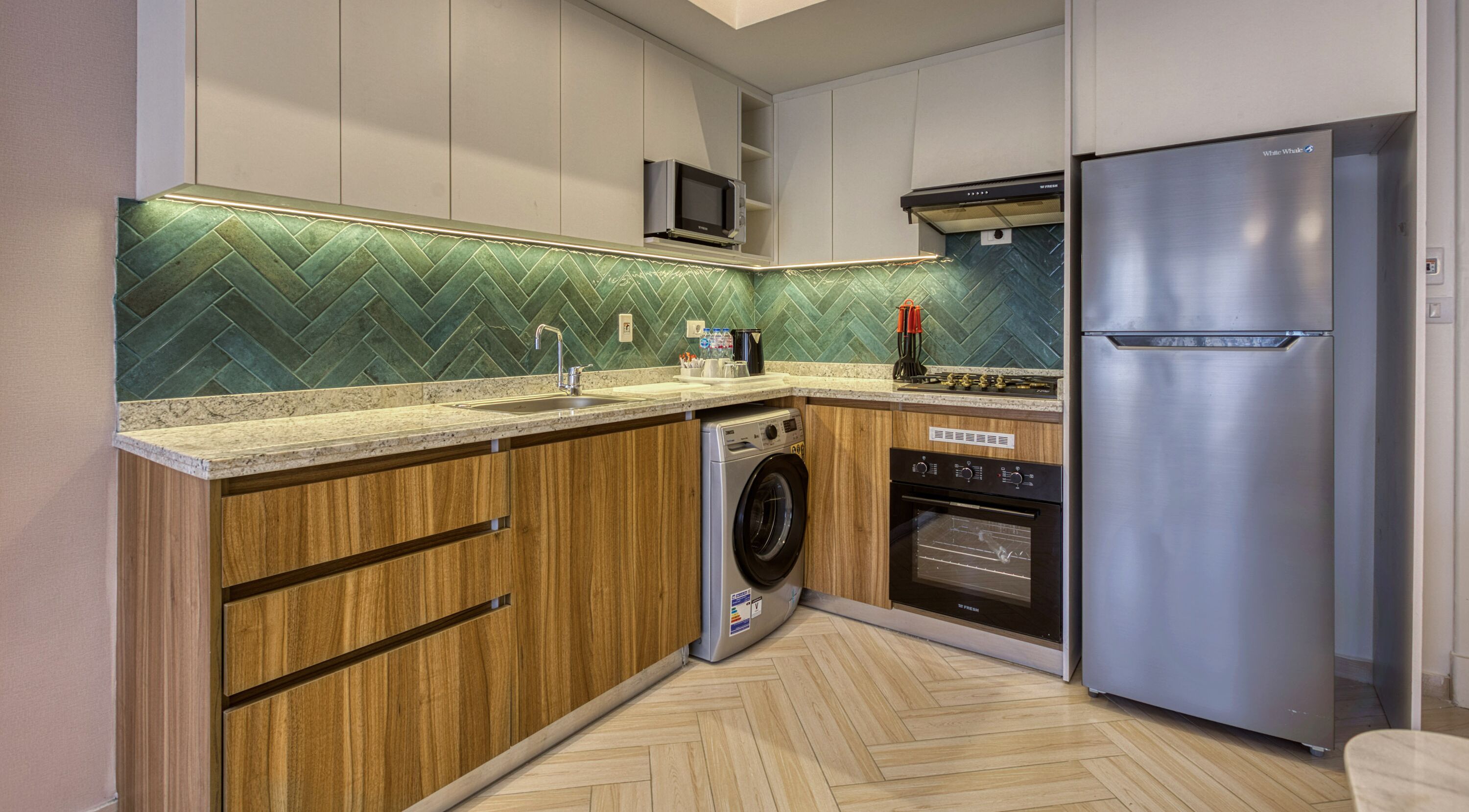 Una cocina compacta con lavadora, horno integrado y refrigerador de acero inoxidable.