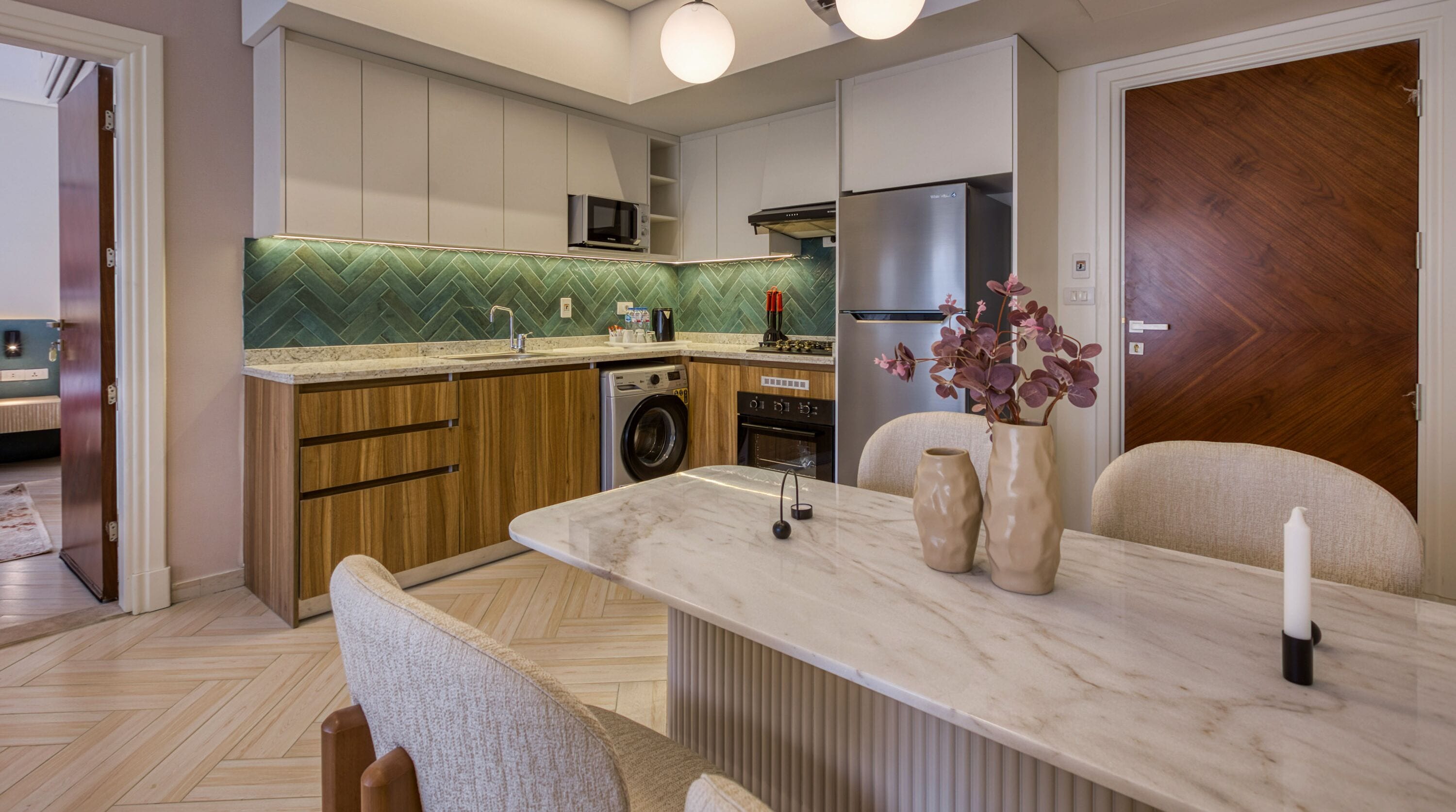 A modern kitchen with wooden cabinets, a built-in microwave, a stainless steel refrigerator, and a dining area with a marble countertop.