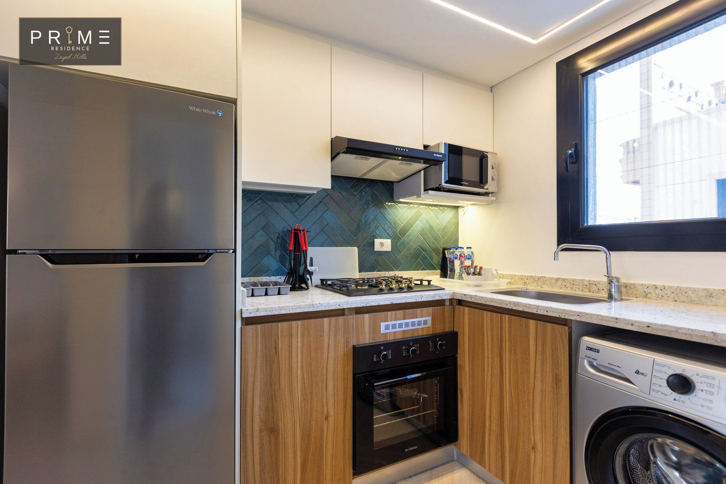 A modern kitchen with stainless steel appliances, wooden cabinets, a microwave, a dishwasher, and a window providing natural light.