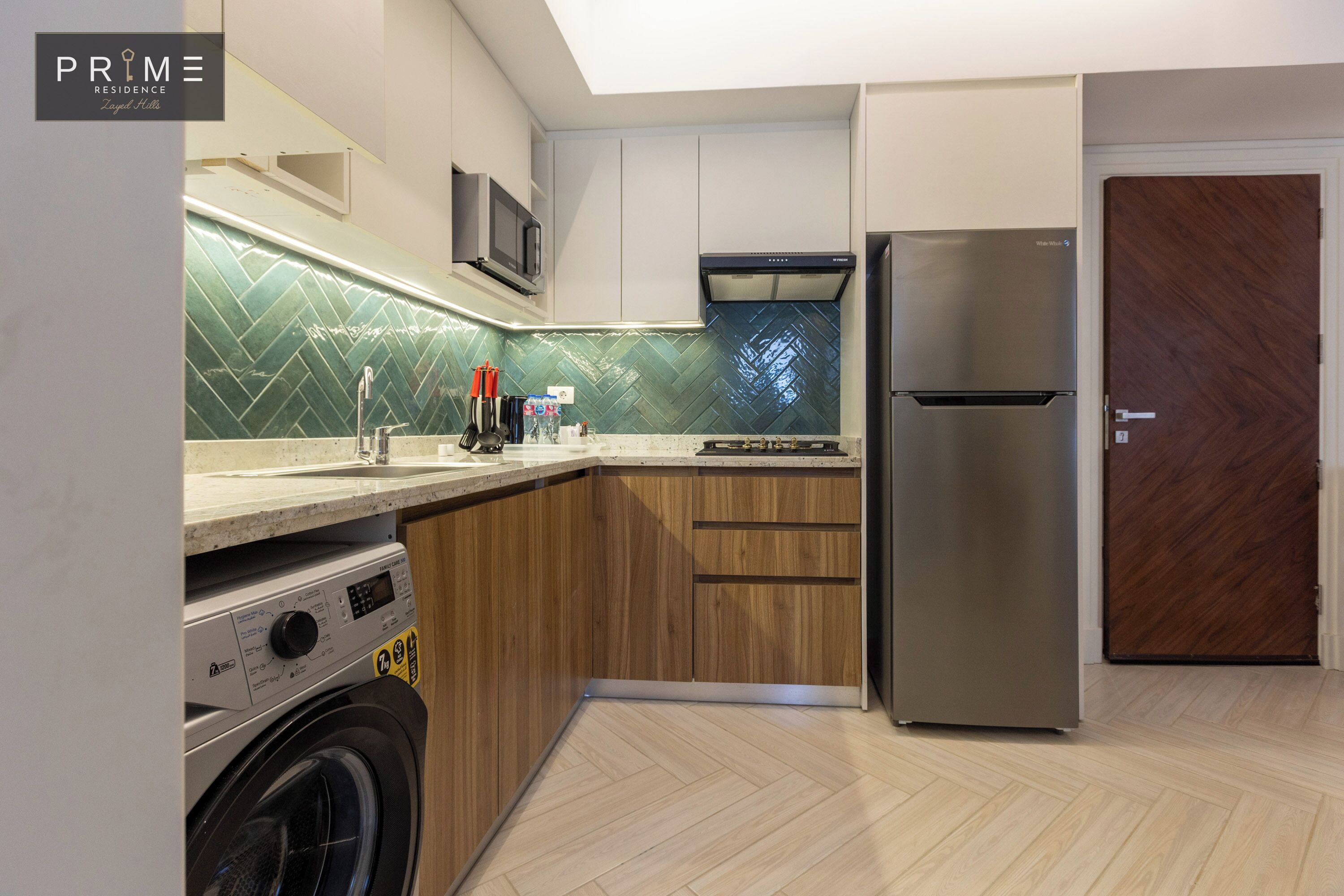 Une cuisine moderne équipée d’un réfrigérateur en acier inoxydable, de meubles en bois, d’un four à micro-ondes et d’un lave-linge.