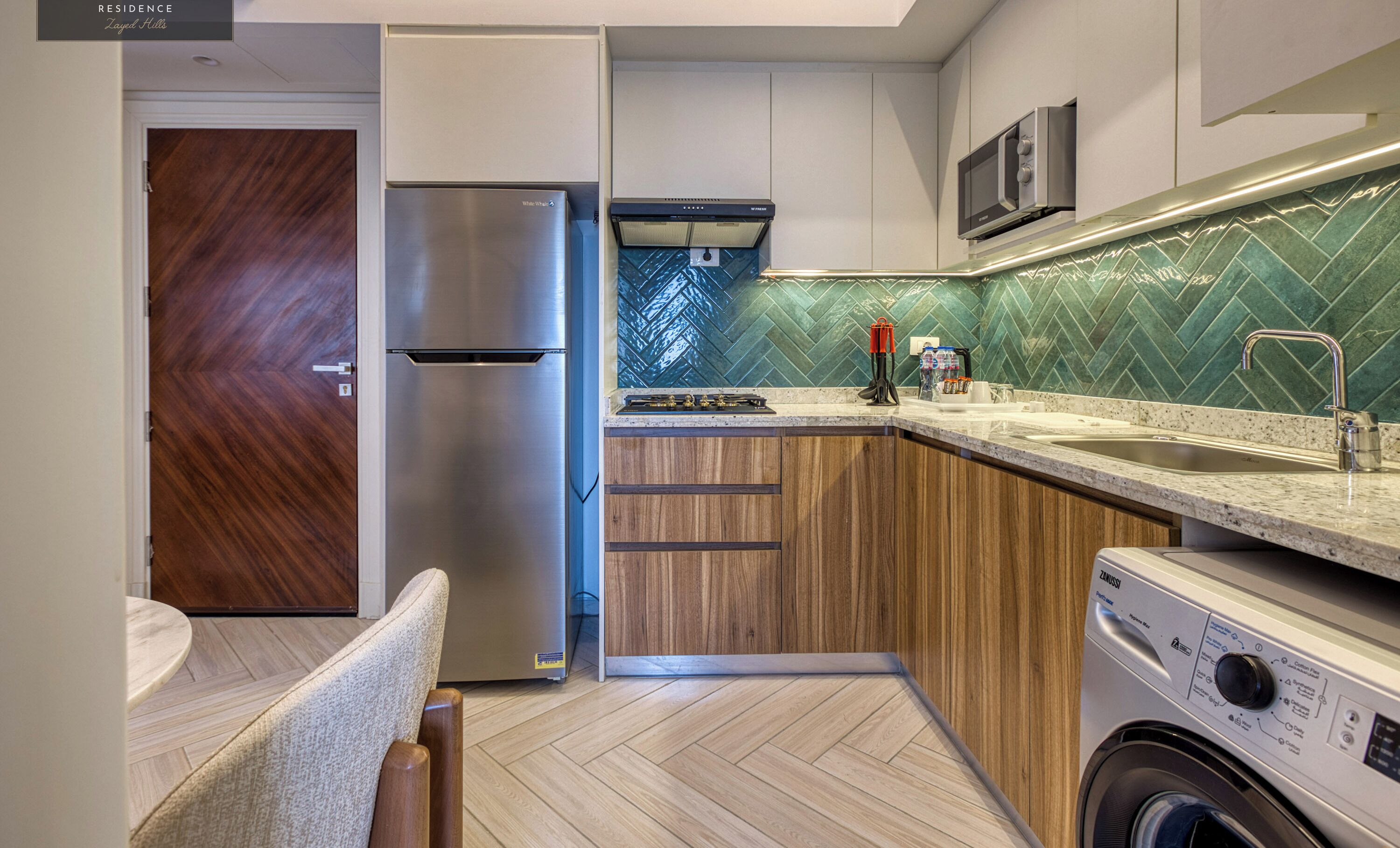 Una cocina moderna con lavadora y secadora integradas, armarios de madera y salpicadero de baldosas en espiga.