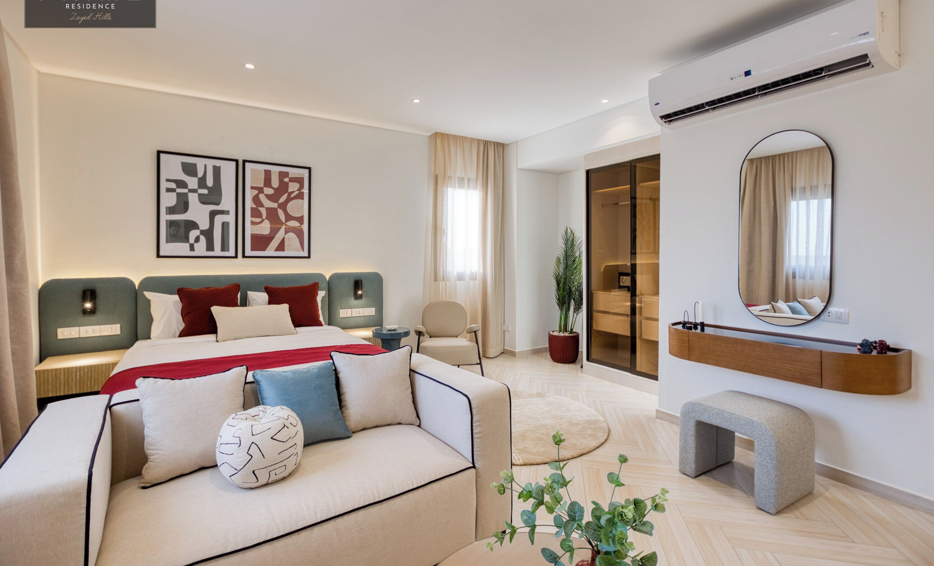 A modern hotel room with a large bed, a sofa, a mirror, and a potted plant.