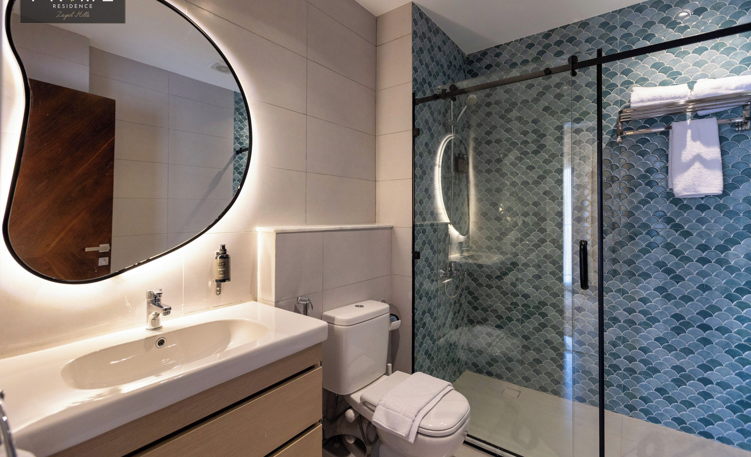 A modern bathroom with a large mirror, a sink, a toilet, and a glass-enclosed shower.