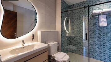 A modern bathroom with a large mirror, a sink, a toilet, and a glass-enclosed shower.