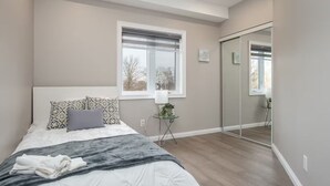 A bedroom with a bed, a window, a mirror, and a small table with a plant. - The Simple Escape (Kitchener)