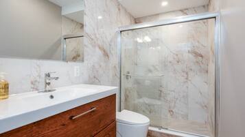 A bathroom with a marble vanity, a glass shower enclosure, and a white toilet.