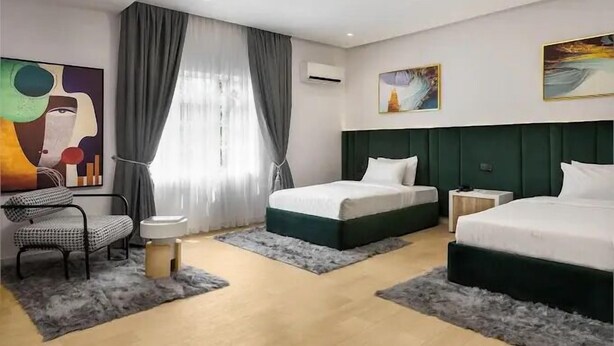 A modern hotel room with two beds, a seating area, and artwork on the walls.