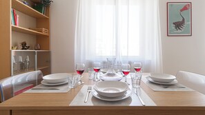 A dining table set with plates, glasses, and cutlery, with a window and curtains in the background. - Italianway Comfort - Maffei 20 (Milan)