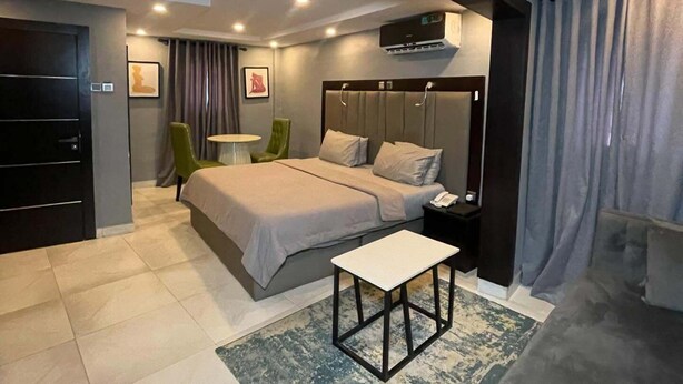 A modern bedroom with a bed, bedside table, and a small seating area. - Noir by Fortys (Lagos)