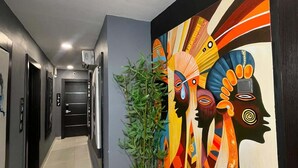 A hallway with a modern design, featuring a vibrant abstract mural on the wall, a potted plant, and a series of doors with numbers. - Noir by Fortys (Lagos)