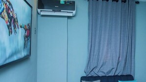 A modern living room with a blue sofa, a white side table, and a large air conditioning unit mounted on the wall. - Noir by Fortys (Lagos)