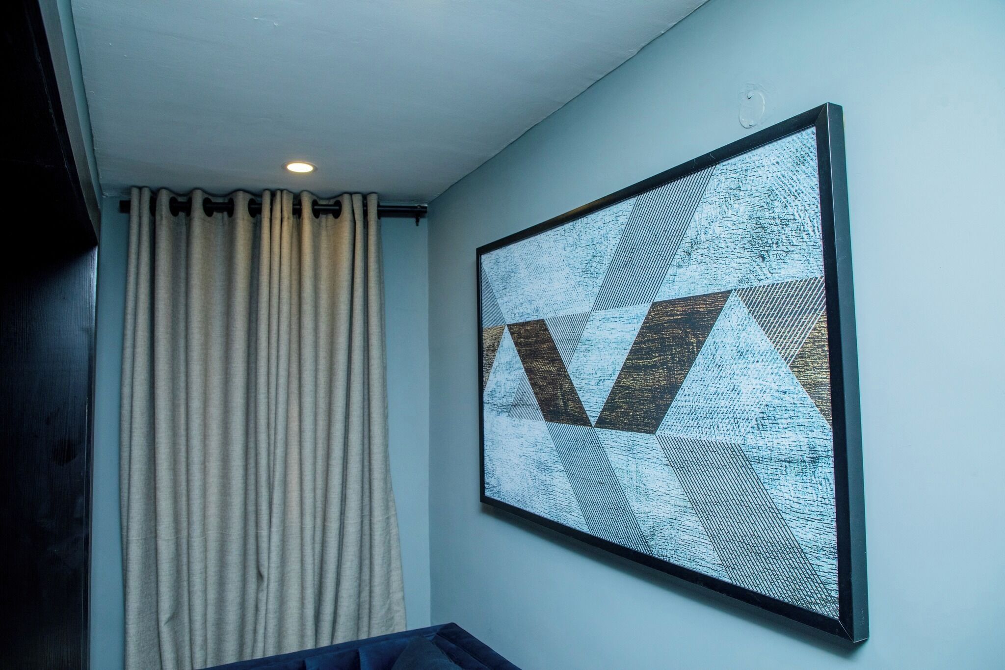 A room with a large abstract painting on the wall, a window with curtains, and a ceiling light.