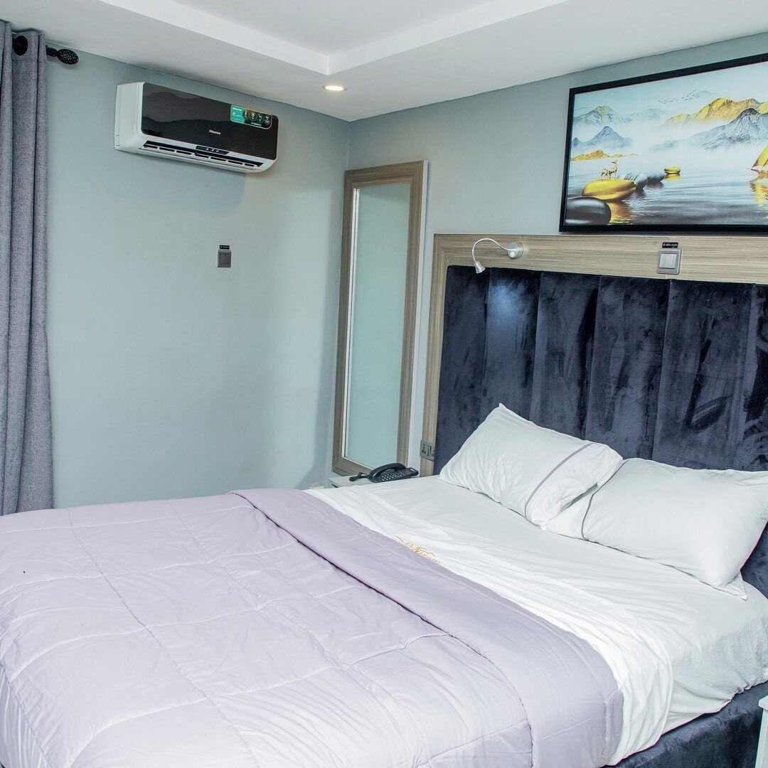 A bedroom with a bed, a large mirror, an air conditioning unit, and a painting on the wall.