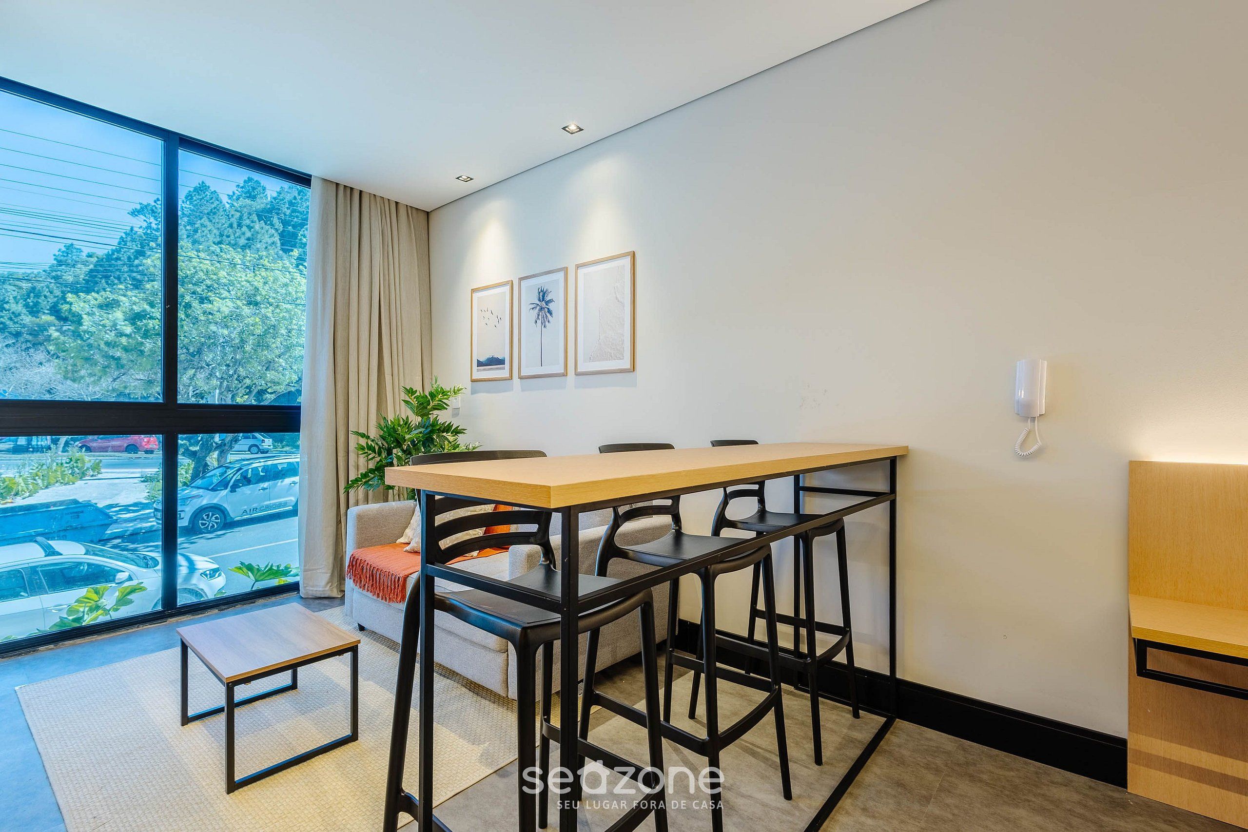 A modern room with a large window, a dining table with chairs, a sofa, and a small table.
