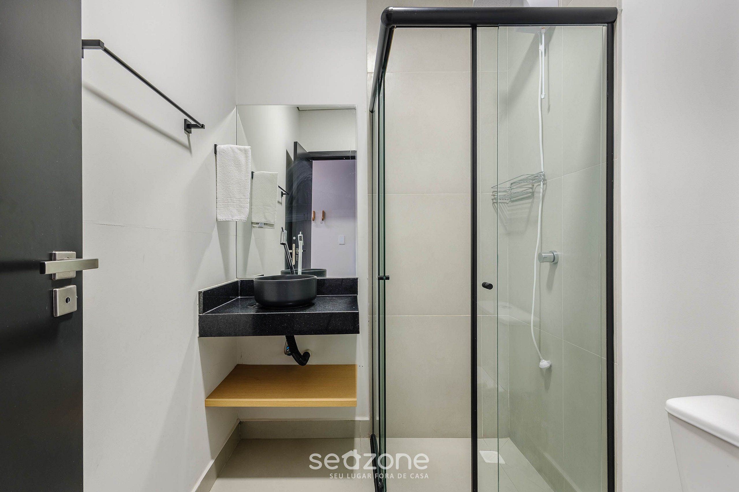 A modern bathroom with a glass-enclosed shower, a black countertop with a sink, and a wooden shelf.