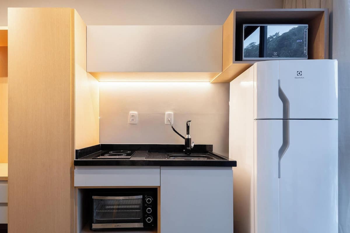 A compact kitchen with a built-in oven, a refrigerator, and a small TV mounted on the wall.