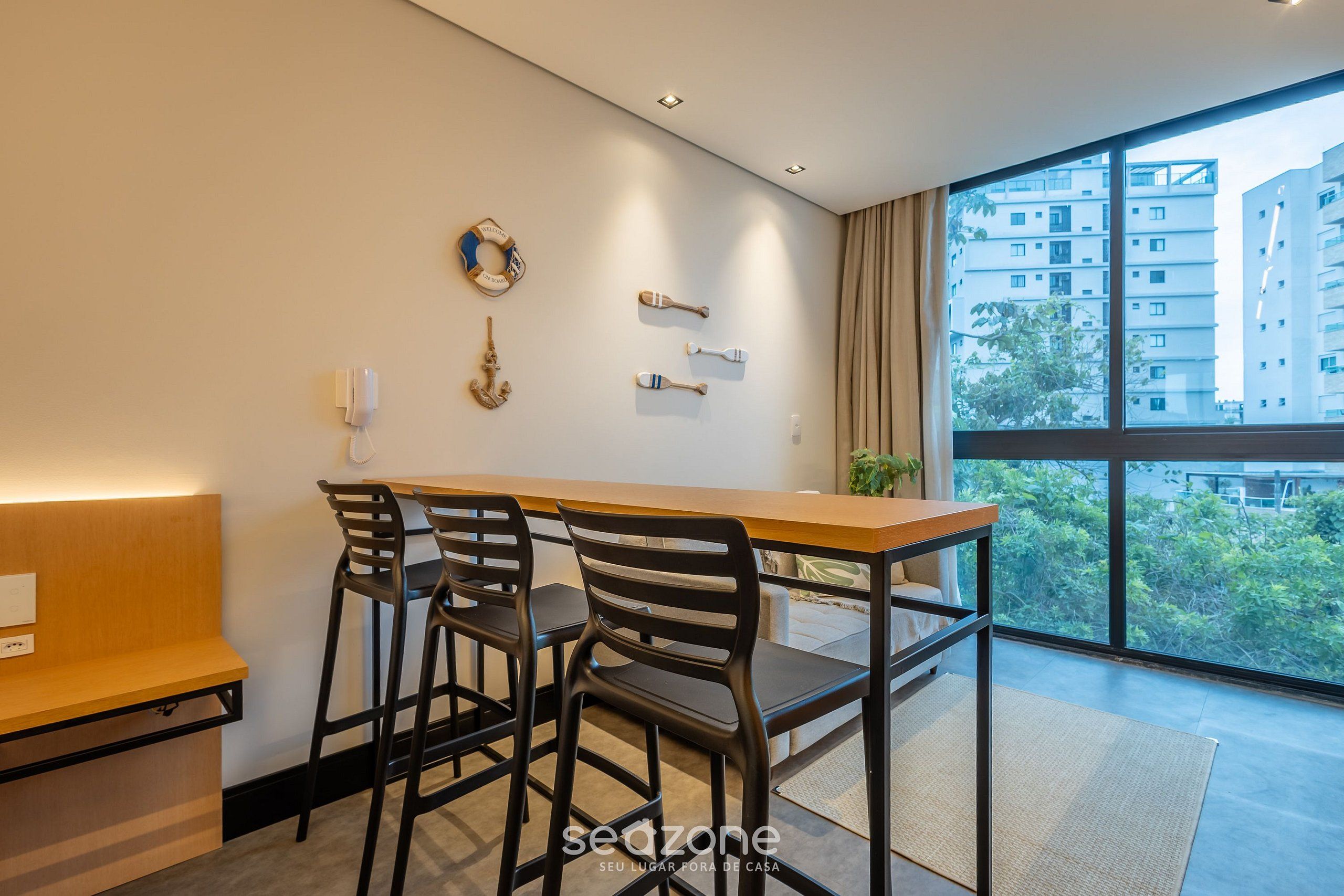A modern room with a wooden table and black chairs, a large window with a view of buildings, and a wall with nautical decor.