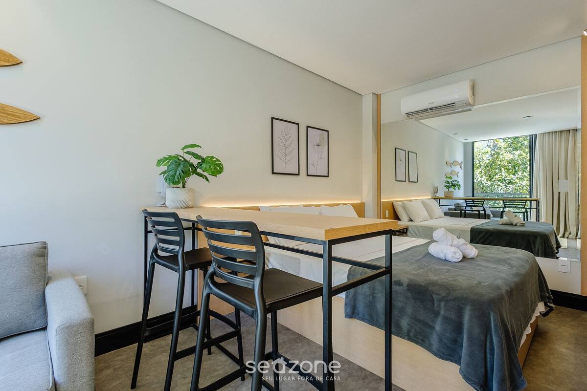 A hotel room with a bed, a desk with two chairs, a potted plant, and artwork on the wall.
