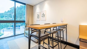 Un comedor moderno con una mesa grande y sillas, un sofá, y vistas a la vegetación a través de amplias ventanas.