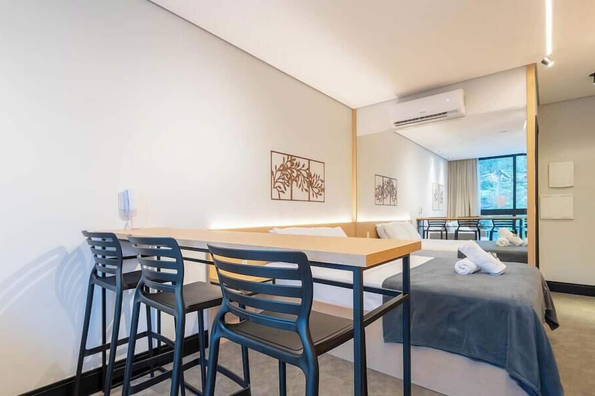A hotel room with a bed, a desk with chairs, a small table, and artwork on the walls.