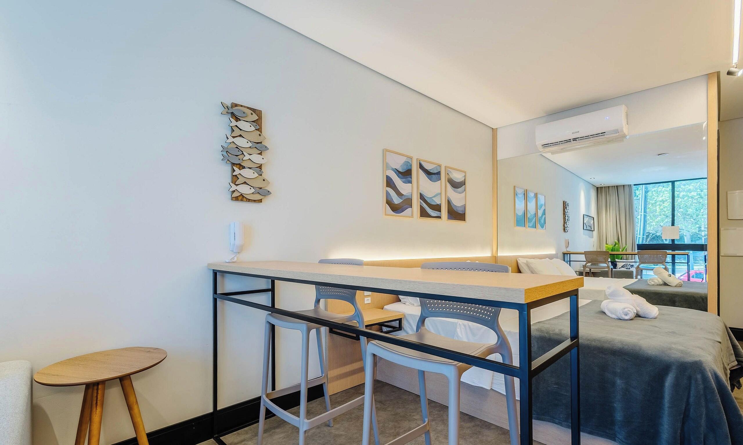 A modern hotel room with a bed, a desk with chairs, and artwork on the walls.